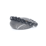 Black beaded bracelet on a gray stone surface with a white background