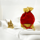 Red and gold potli bag with a small gold statue on a white fabric.
