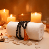Black beaded bracelet with orange tassel on a white towel surrounded.
