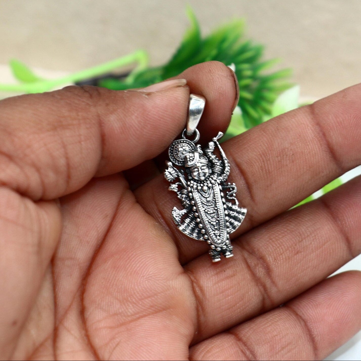 Silver pendant held in a hand with a blurred green plant in the background