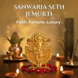 Decorative gold murti with candles and incense on a wooden surface.